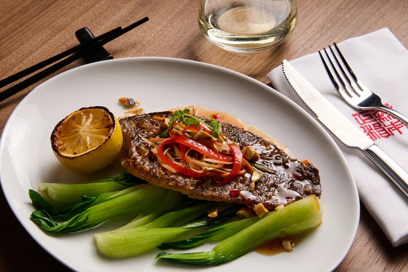 Fresh catch fillet from Holland America Line's Global Fresh Fish Program plated with bok choy, charred lemon and chili garnish at Morimoto by Sea