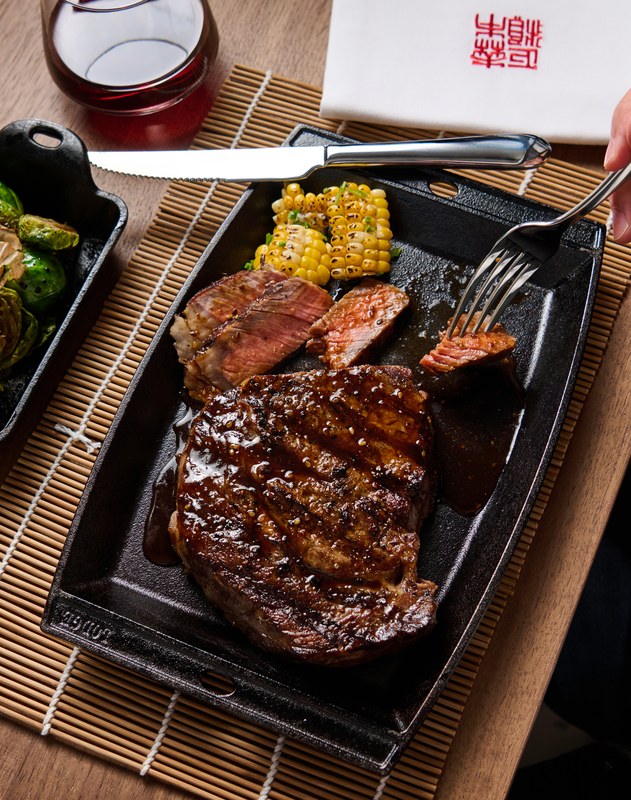 Glazed ribeye steak sliced on a cast iron sizzle plate with charred corn and a skillet of brussels sprouts at Morimoto by Sea