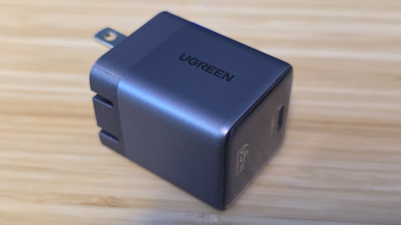 The UGREEN Nexode Air 65W GaN charger sitting on a bamboo desk with its folding prongs extended